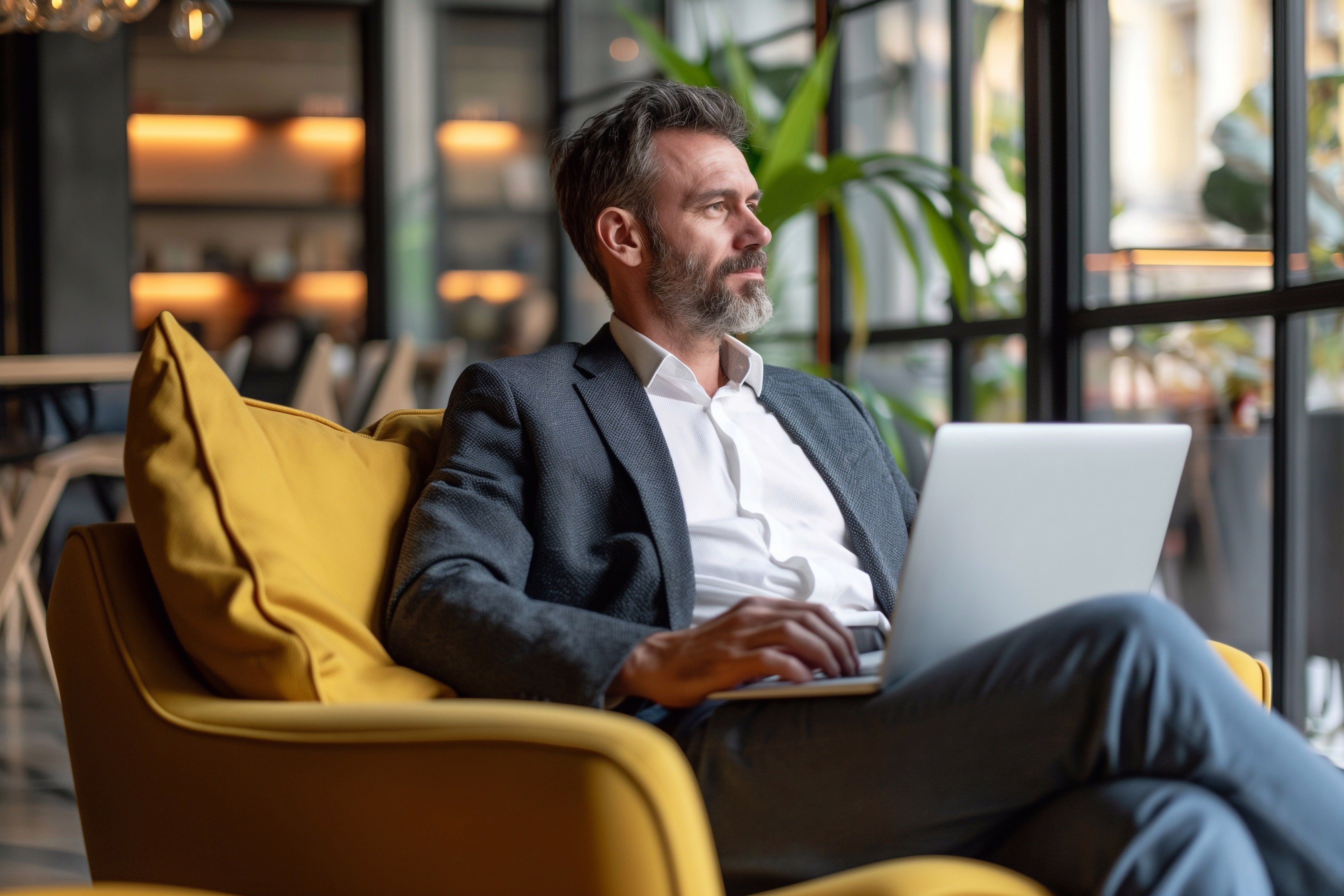 Arbeitgeber sitzt dank digitaler bAV-Beratung entspannt in einem Sessel, mit einem Laptop auf den Knien, und blickt in die Ferne