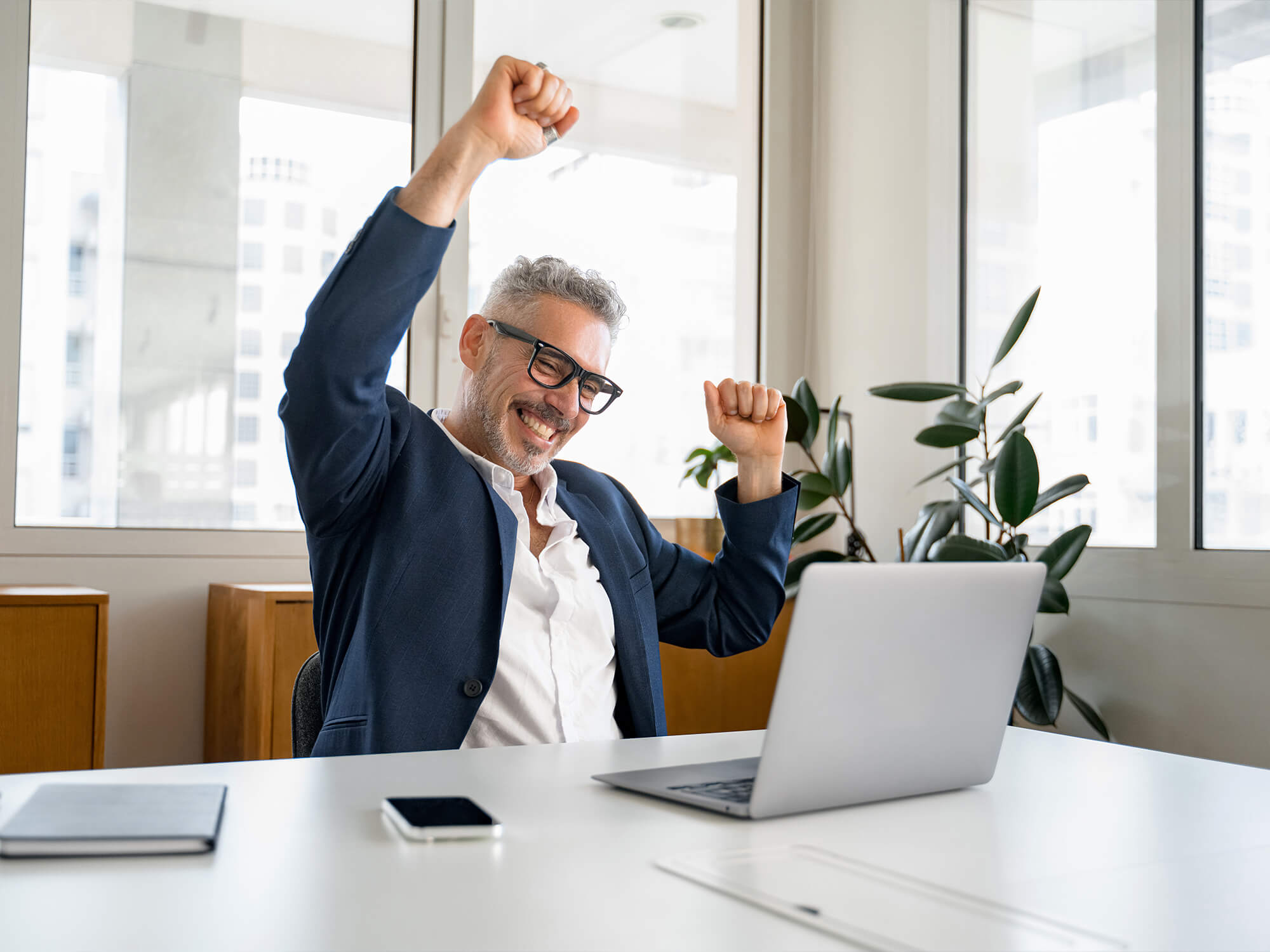 Lachender Versicherungmakler sitzt vor seinem Notebook und reckt die Faust nach oben 