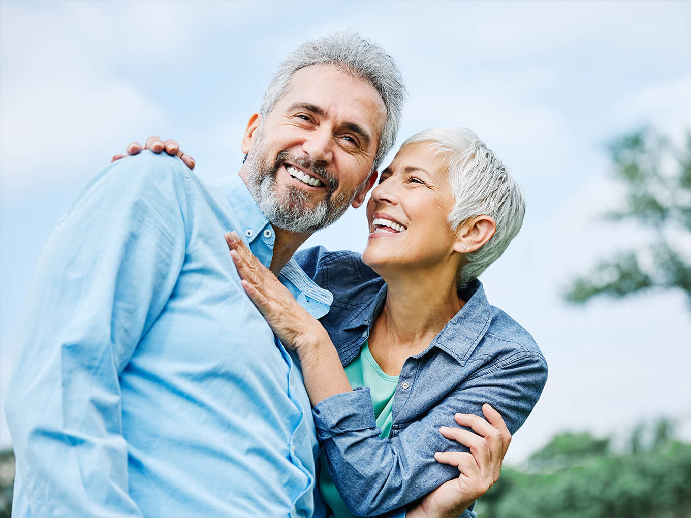 Ein älterer Versicherungsmakler zusammen mit seiner Partnerin in einem Park, die Frau umarmt ihn