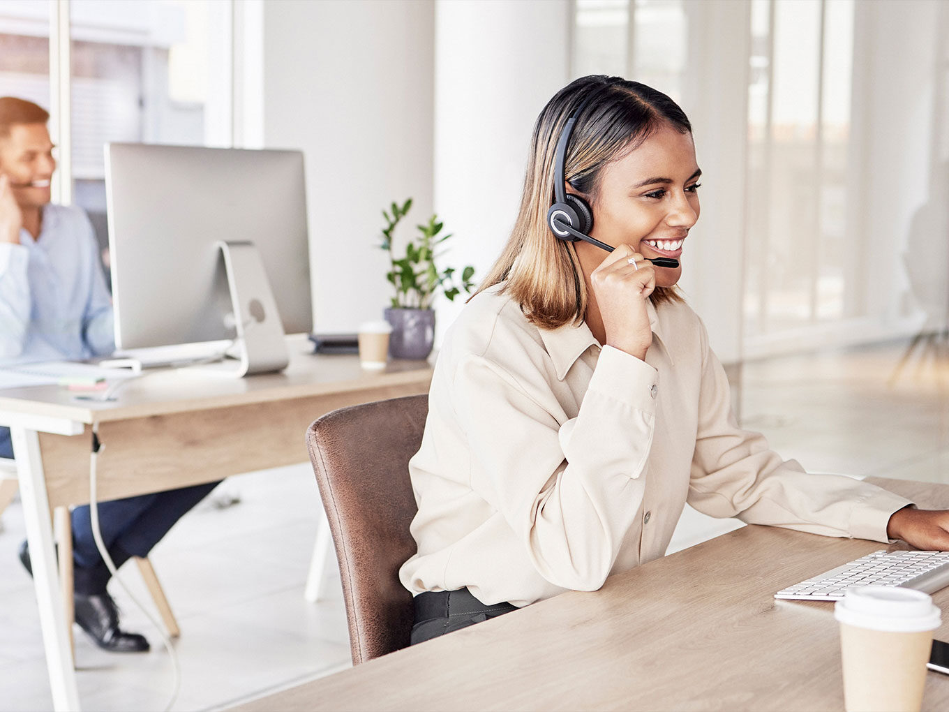 Frau mit Headset sitzt lächelnd am Schreibtisch