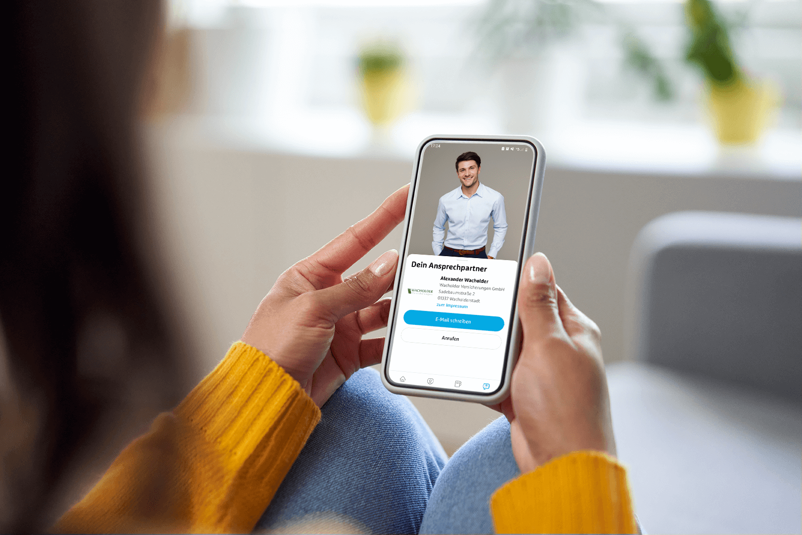 Eine Frau sitzt auf dem Sofa und hält ein Smartphone in den Händen, auf dem die simplr-App mit ihrem Ansprechpartner zu sehen ist